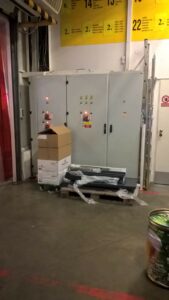 Obrázek ukazuje rozvaděče elektrické energie na pracovišti, které jsou však zabarikádované nějakým balícím materiálem jako jsou krabice, fólie a palety.